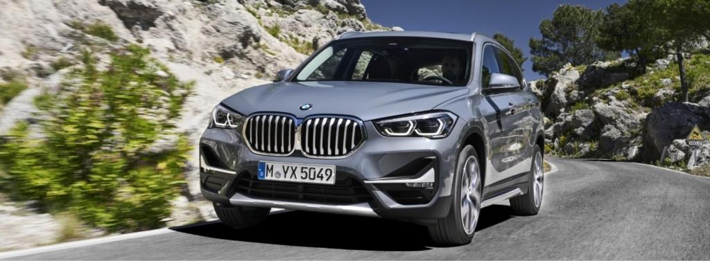 Un BMW X1 gris circulant sur une route sinueuse, entourée de paysages rocheux et verdoyants.